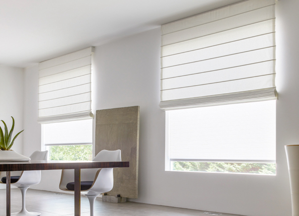 Two large windows featuring Cascade Roman Shades in a dining room with a large wooden plank and table with white chairs