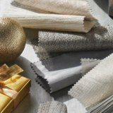 Various metallic fabric swatches from The Shade Store on a grey tabletop with silver and gold ornaments and gift