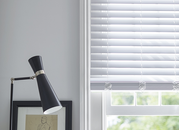 Faux Wood Blinds in Blanc match the white walls of a bathroom with contrasting black decor including a lamp and picture frame