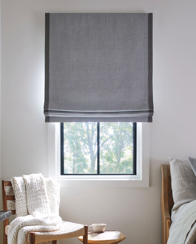 A cozy farmhouse-style bedroom window featuring a motorized Flat Roman Shade in Baldwin stone fabric.