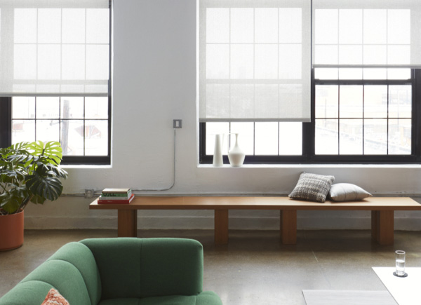 A bright modern room has a green couch, low wood bench and windows with Solar Shades made of Chilewich Boucle in Newsprint