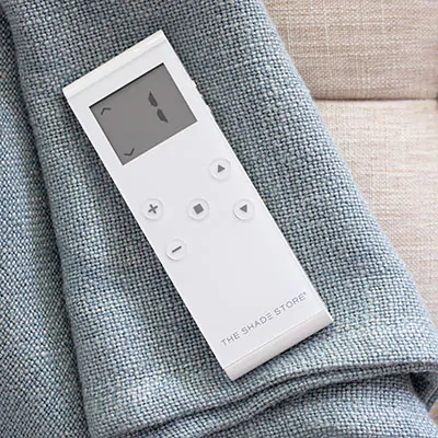 A motorization remote lays on a piece of fabric suggesting how to close blinds with a motorization control system
