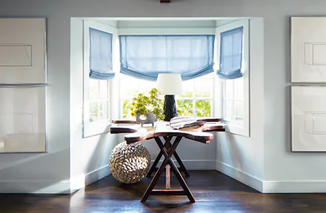 Relaxed Roman Shades made of Holland and Sherry Andes wool in Azure are used in place of blinds for bay window in a coastal nook