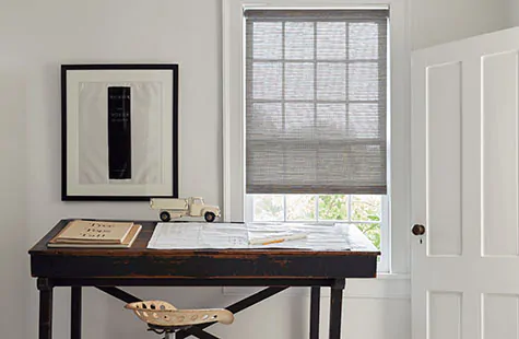 Bamboo roller blinds made of Roller Shades in Jackson, Sand, cover a small window in an office with a dark wood table