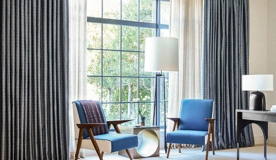 Two layers of Tailored Pleat Drapery made of Breeze in Sand and Vanda in Midnight adorn a large window in a sitting area as layered window treatments for privacy and light control
