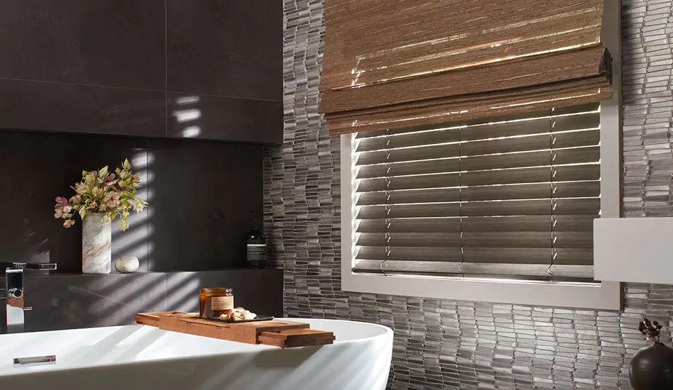 A dark calm bathroom has Wood Blinds made of 2-inch Bamboo in Black layered with a Woven Wood Shade made of Del Rey in Taupe as layered window coverings for adjustable privacy